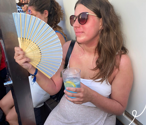 Women with a hand fan holding a drink and eczema on her face